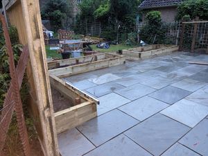 A large patio paved with sandstone and bordered by timber raised beds.