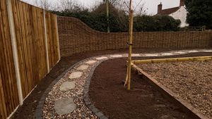 A paving path between stacked sleepers and conifer hedges